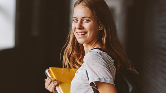 Rear view of beautiful girl walking through university hallway looking back and smiling. female student going for the lecture.