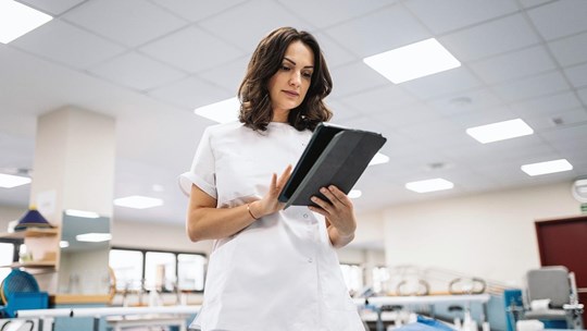 Low angle of brunette in medical uniform browsing data on digital tablet while working in spacious physiotherapy room of modern clinic